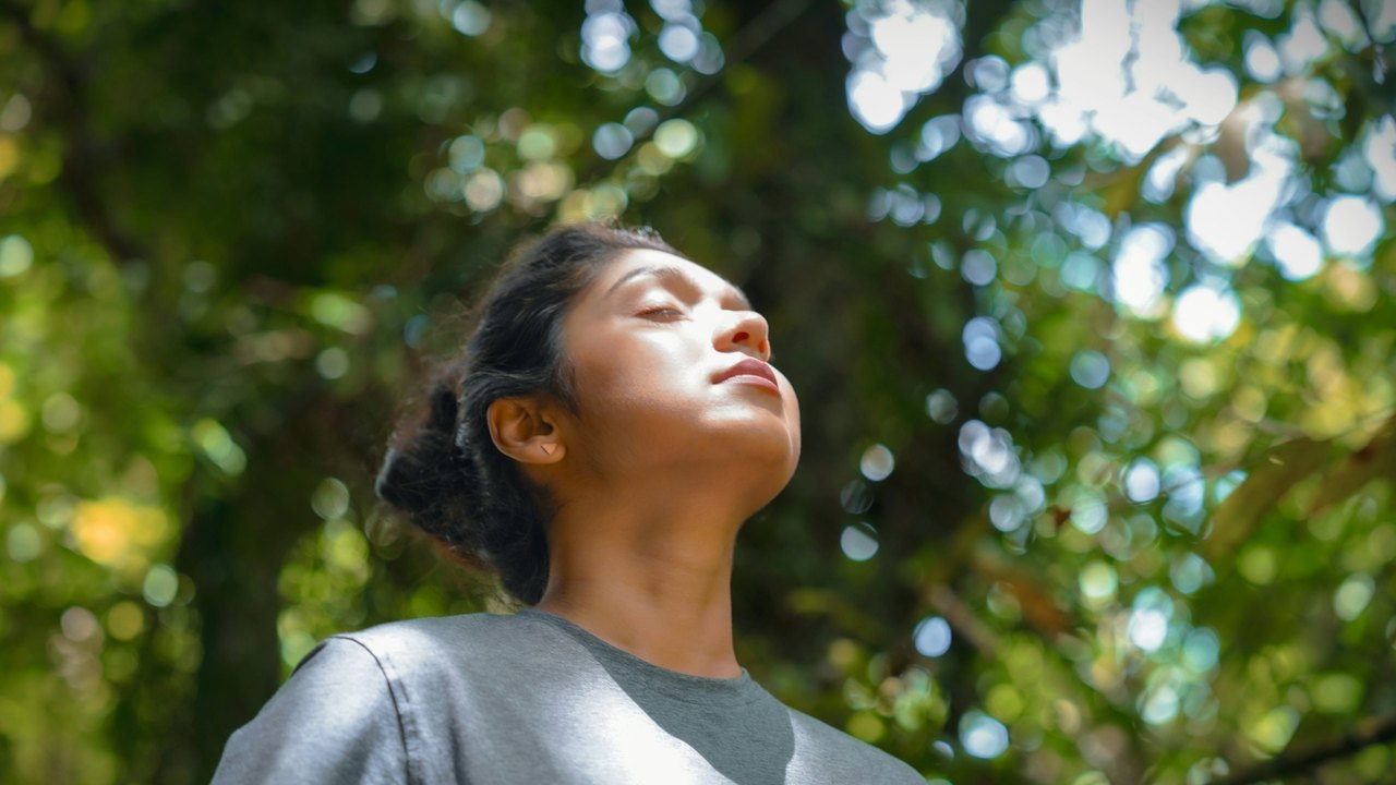 Woman taking a deep breath of fresh air beneath sunlit trees
