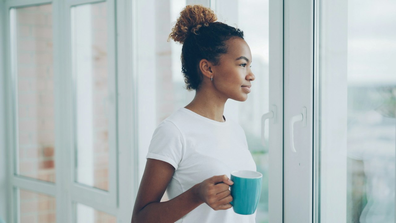 Woman holding a mug and looking out of a bright window at home