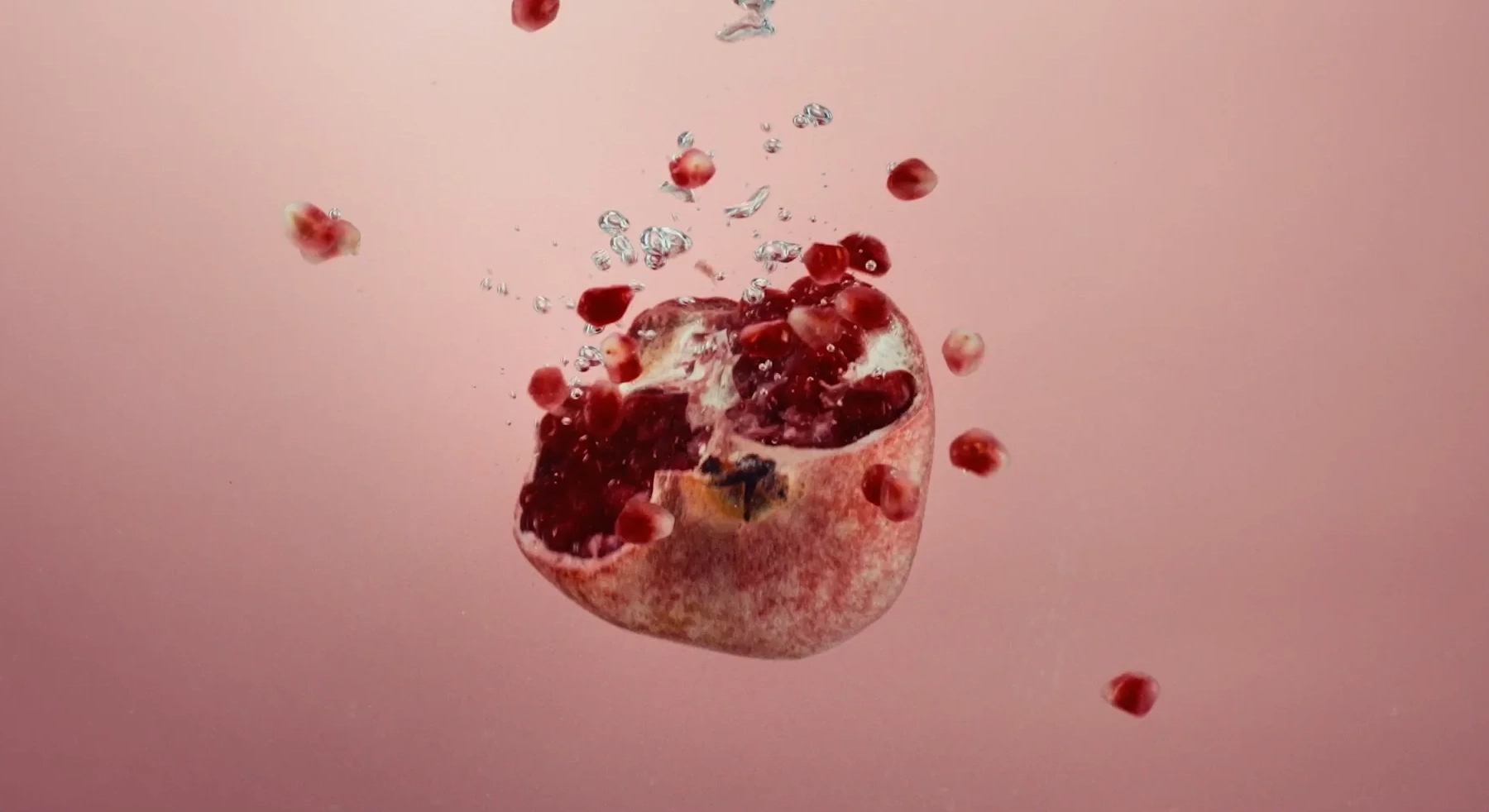 Grenade ouverte en suspension avec des grains rouges et des bulles dans un liquide rose.
