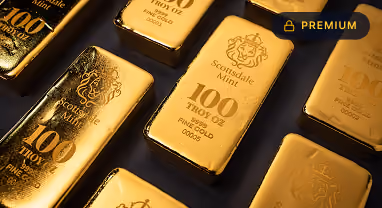 Several shiny 100 troy oz Scottsdale Mint fine gold bars arranged at angles on a dark surface.
