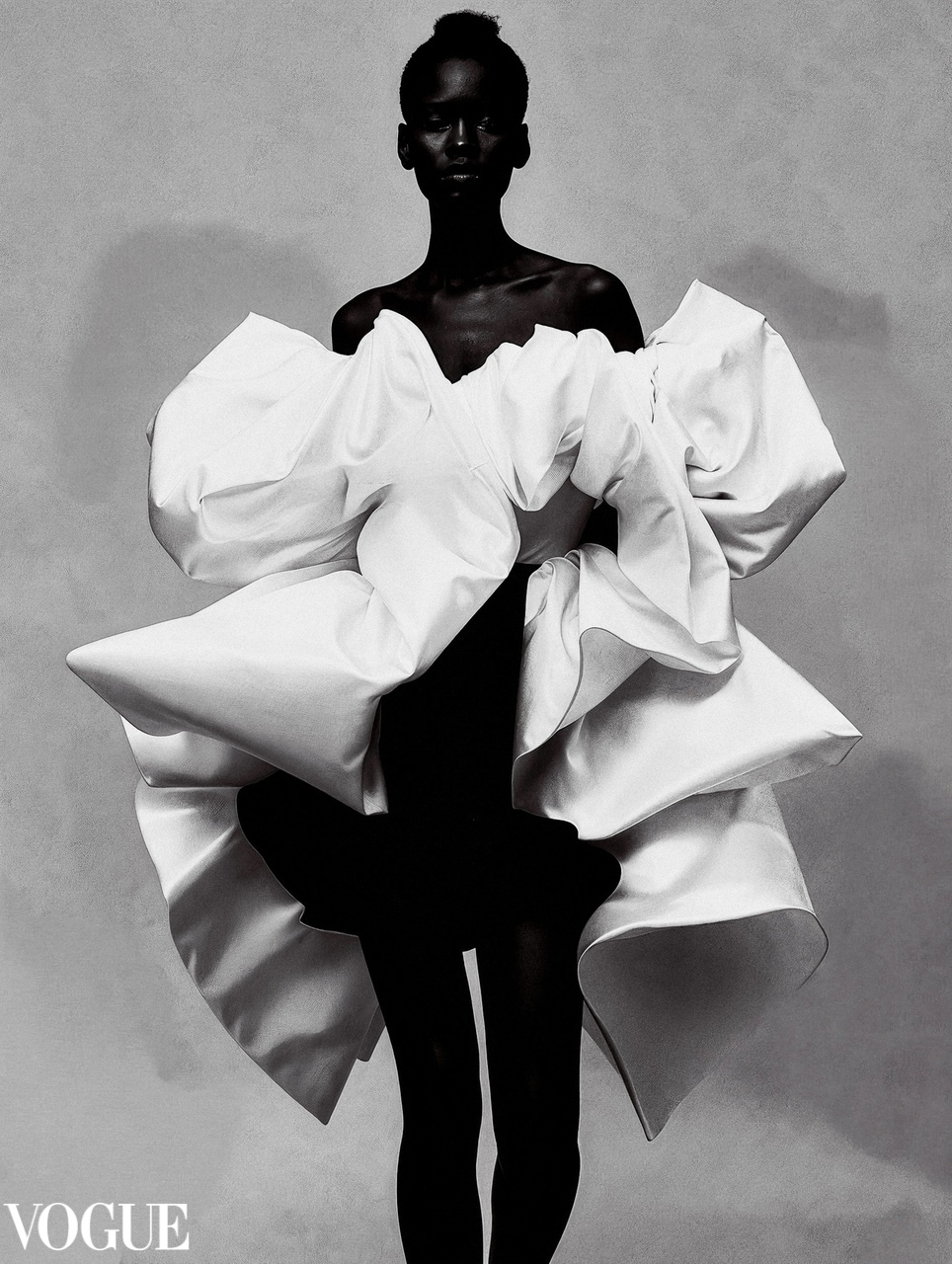 Fashion model wearing an avant-garde white voluminous dress with large sculptural folds against a neutral background.
