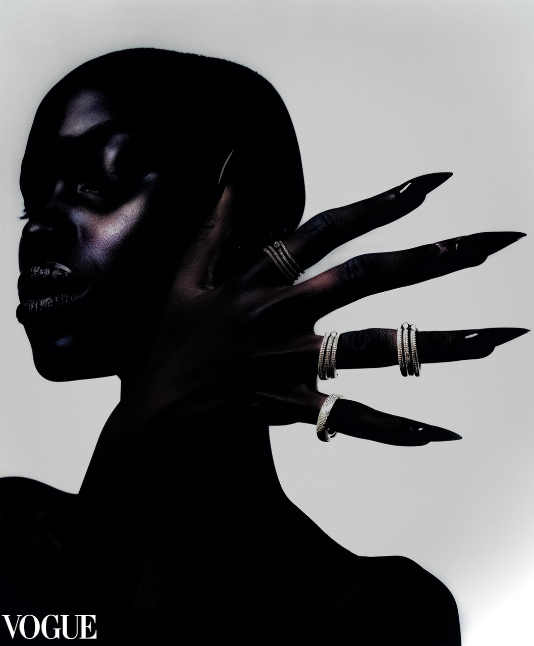 High-contrast silhouette of a person with hand raised near face, adorned with multiple textured rings and long pointed nails.