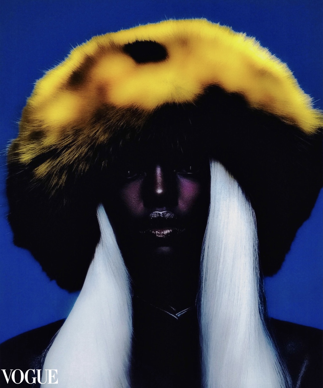 Model with dark skin wearing a large yellow and black fur hat and long white hair against a blue background.