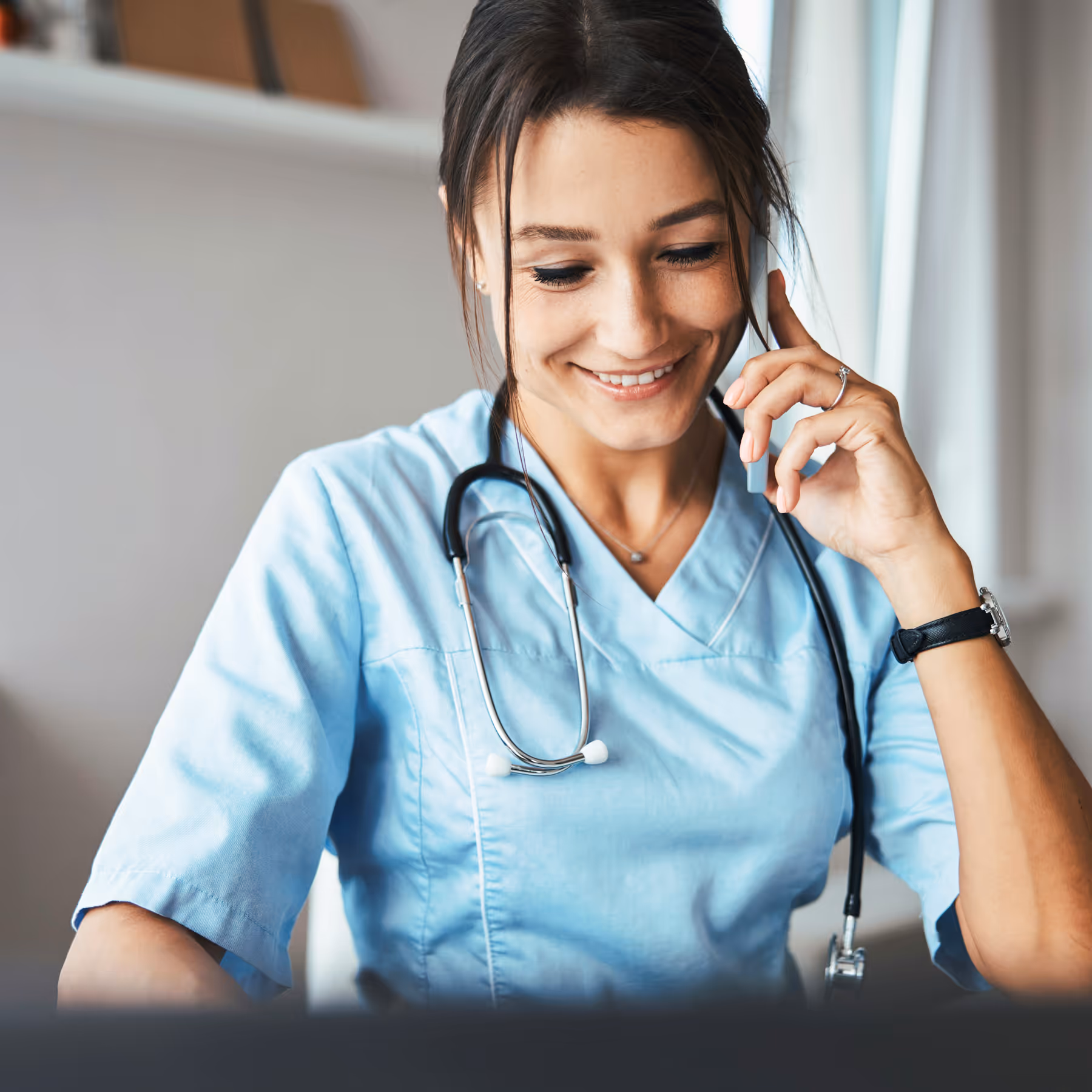 Smiling female doctor in blue scrubs talking on a phone.