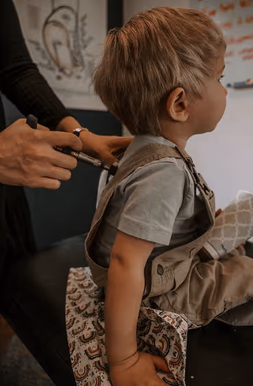 Child sitting on an exam table while a healthcare provider examines their back with a tool.