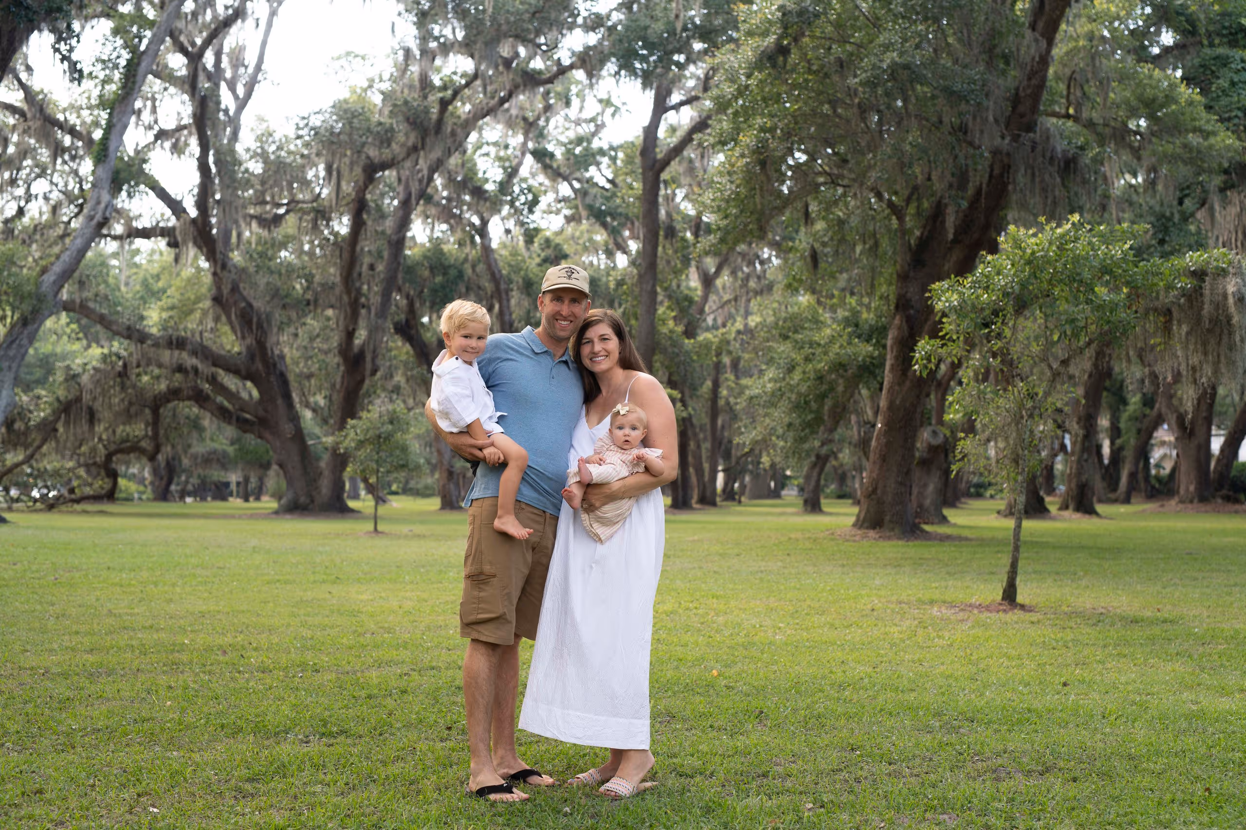 Smiling family standing close in a green park with large trees and grass