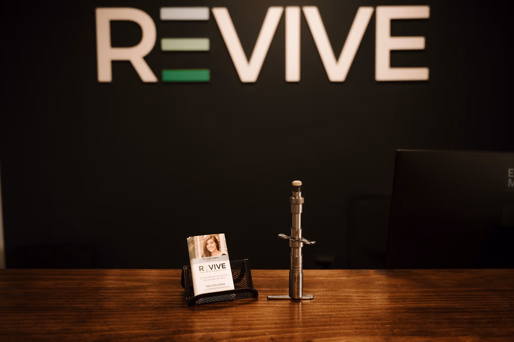 Business cards and a chiropractic adjustment tool on a wood counter with RE-VIVE sign in background.