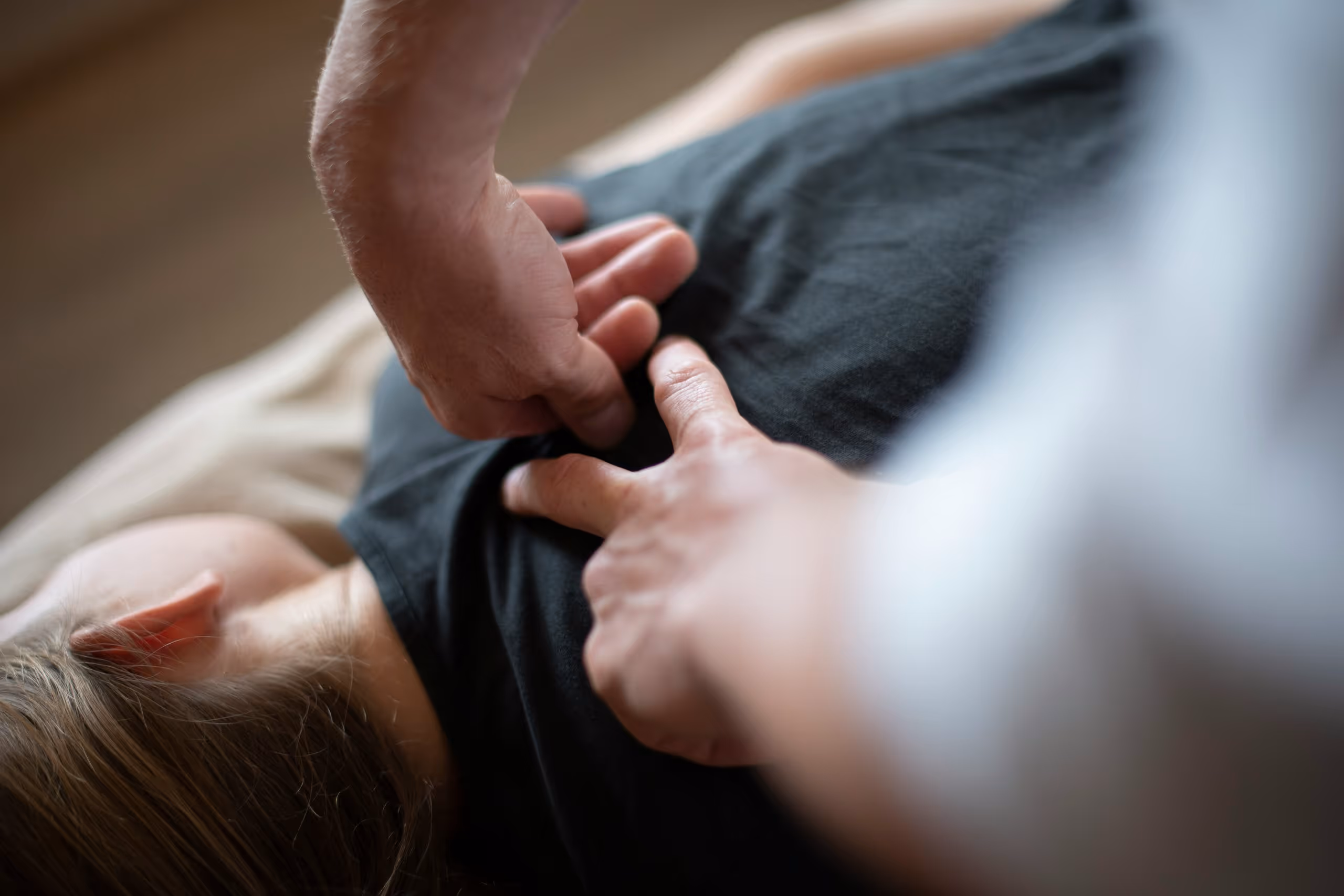 Hands giving chiropractic treatment on upper back of a person lying down on stomach.