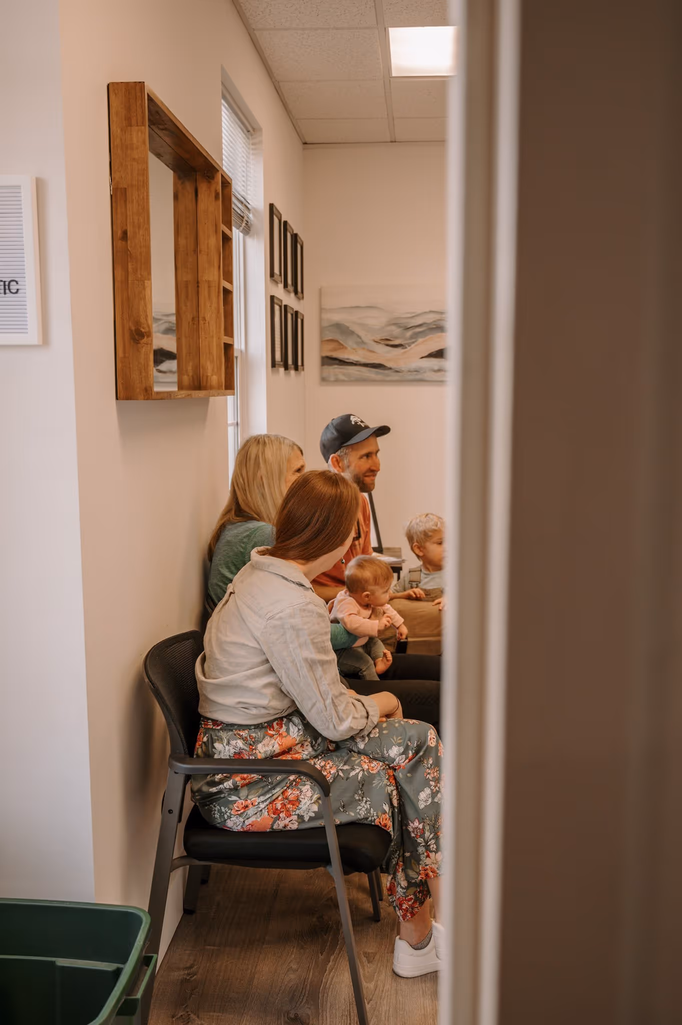 Family with two adults and two young children sitting in a cozy waiting room with wall art.
