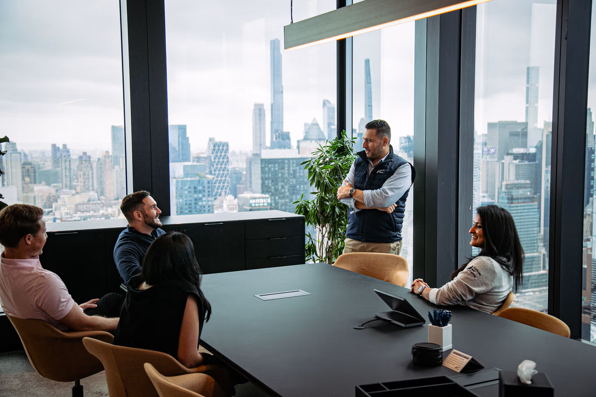 Five professionals having a meeting in a modern office with large windows showing a city skyline.