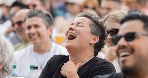 Group of diverse people laughing and enjoying an outdoor comedy event together.