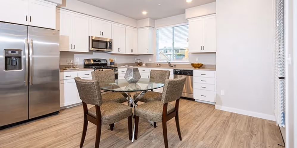 Kitchen with island, white cabinets, and stainless steel appliances featuring dining table with chairs