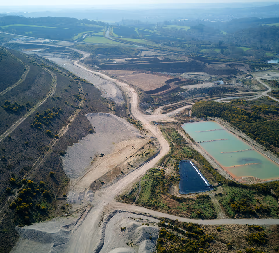 Aerial view of a large mining or excavation site with dirt roads, terraced land, and two rectangular water ponds.