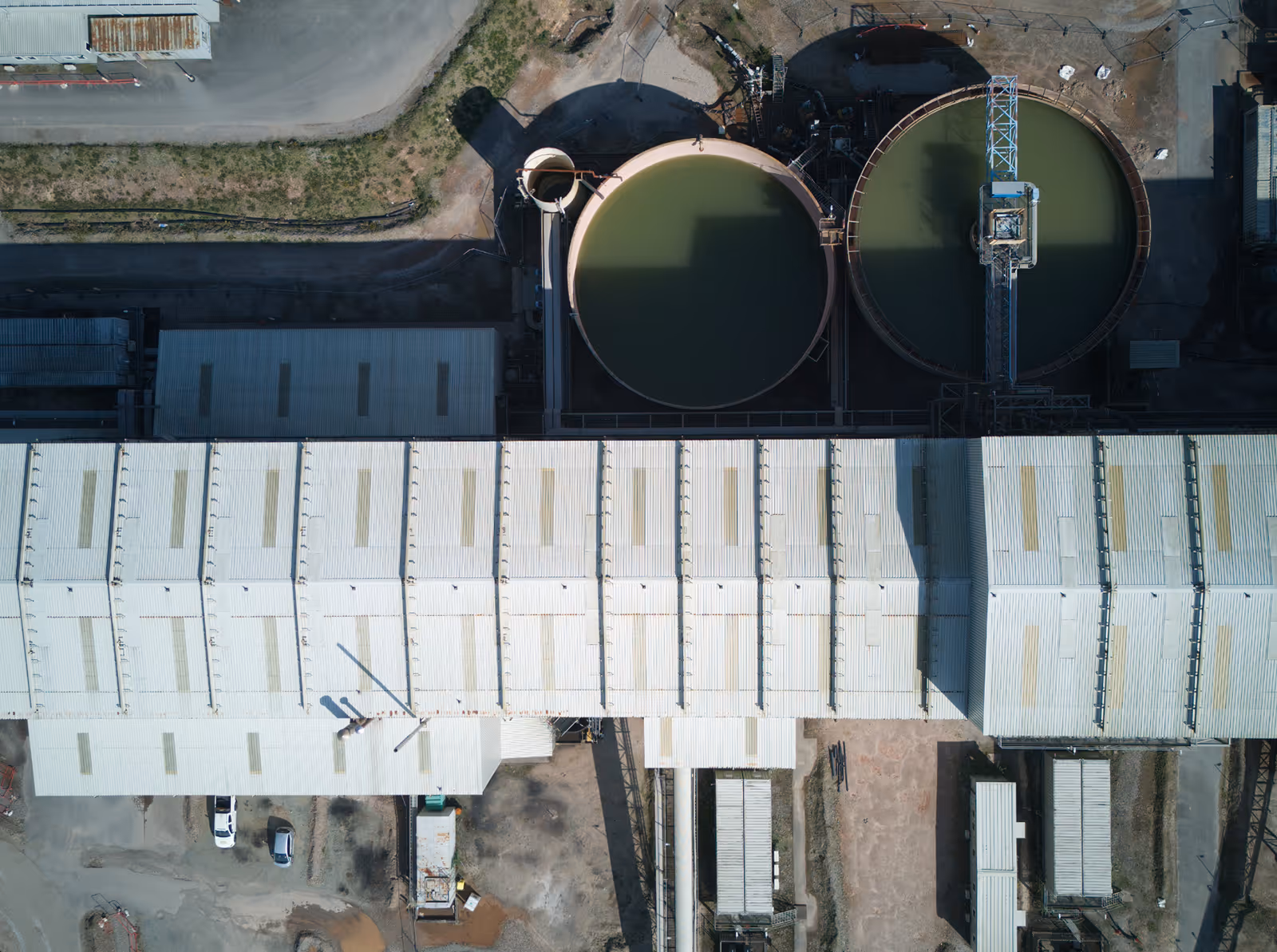 Aerial view of an industrial facility with two large circular tanks containing greenish liquid and a long white roofed building.