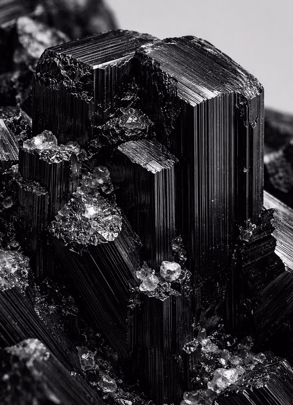 Close-up of black crystalline mineral with shiny, striated surfaces and scattered translucent mineral fragments.