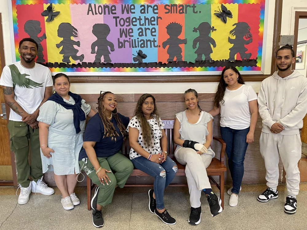 School aides posing together in front of a colorful bulletin board