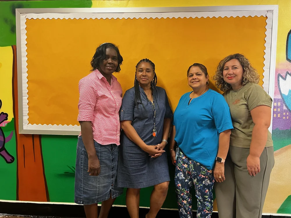 Four school staff members posing together in front of colorful hallway mural