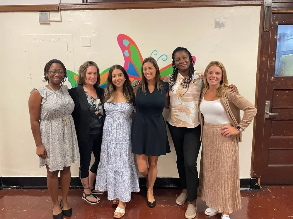 Six kindergarten staff members posing together in front of butterfly mural