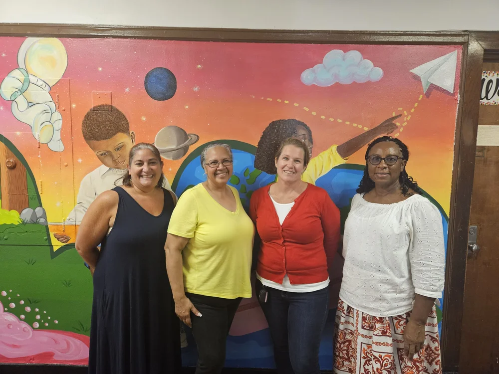 Four school staff members smiling in front of colorful hallway mural