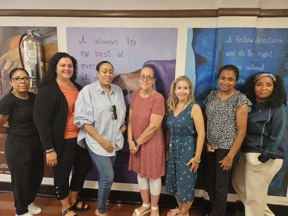 Seven school staff members posing in front of student murals