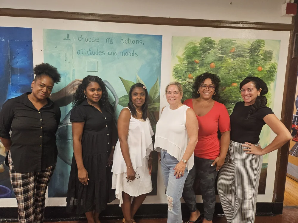 Six school staff members posing in front of hallway mural