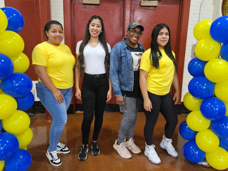 Four staff members posing between blue and yellow balloon columns