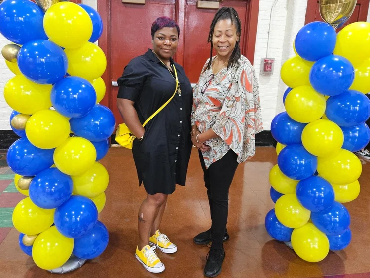 Two staff members posing between blue and yellow balloon columns at school event