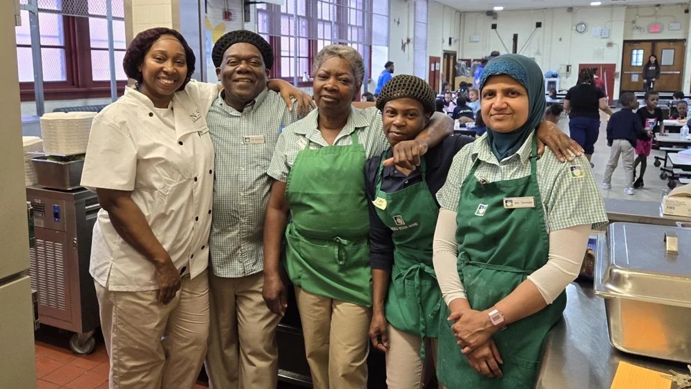 Five school kitchen staff members posing together in school cafeteria