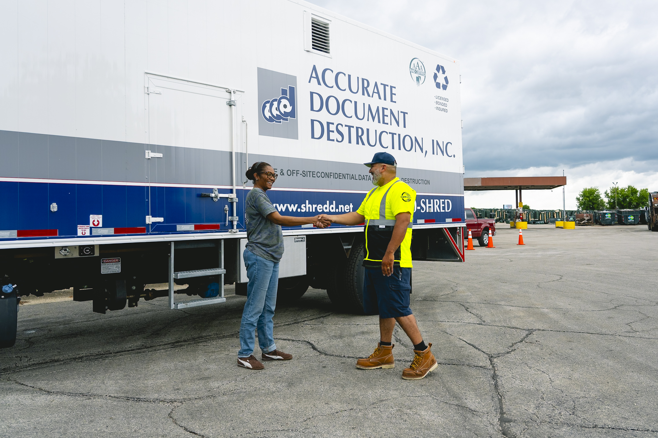 Two people shaking hands outside next to an Accurate Document Destruction truck in a parking lot.