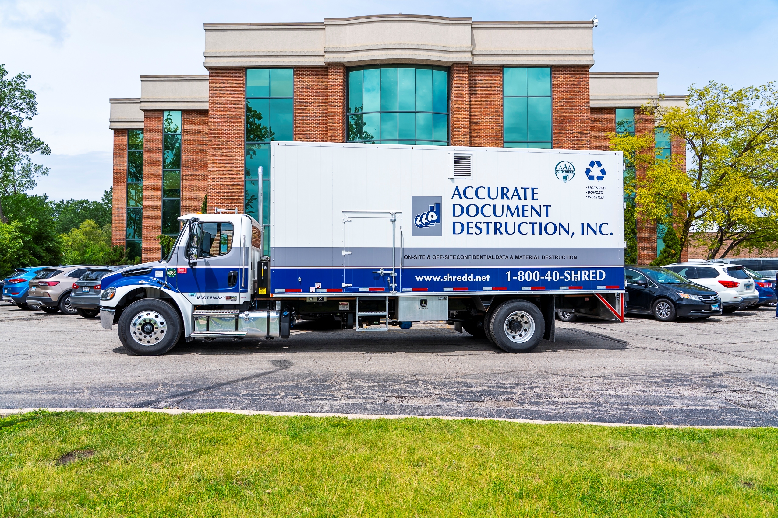 White and blue Accurate Document Destruction truck parked in front of a brick commercial building.