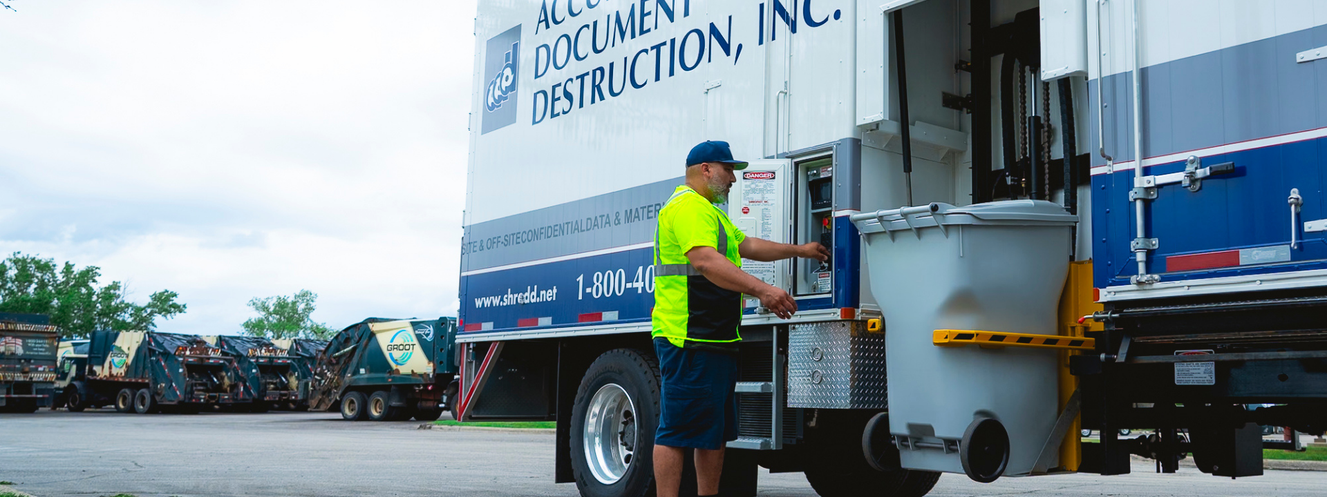 Worker in neon shirt operating a document destruction truck with a large gray bin attached.