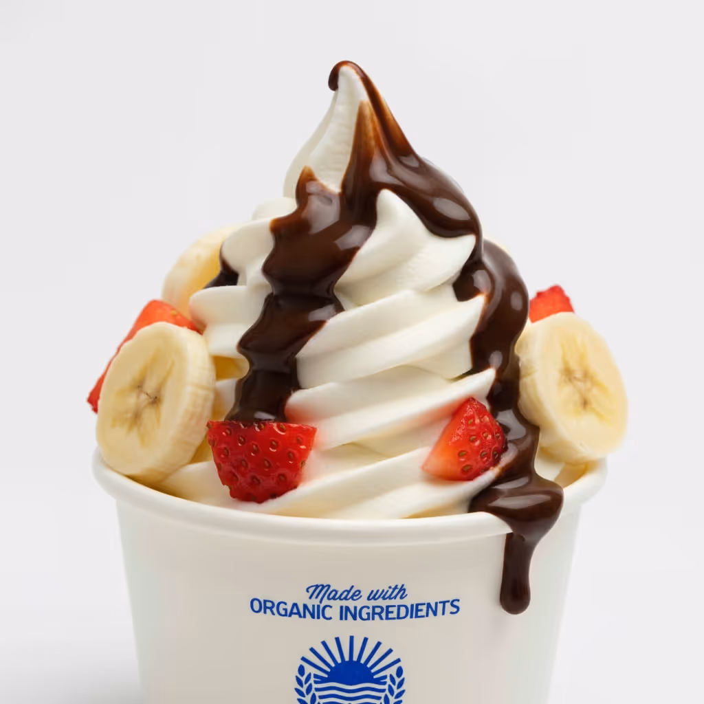 A cup of vanilla soft serve frozen yogurt topped with chocolate syrup, sliced bananas, and strawberries.