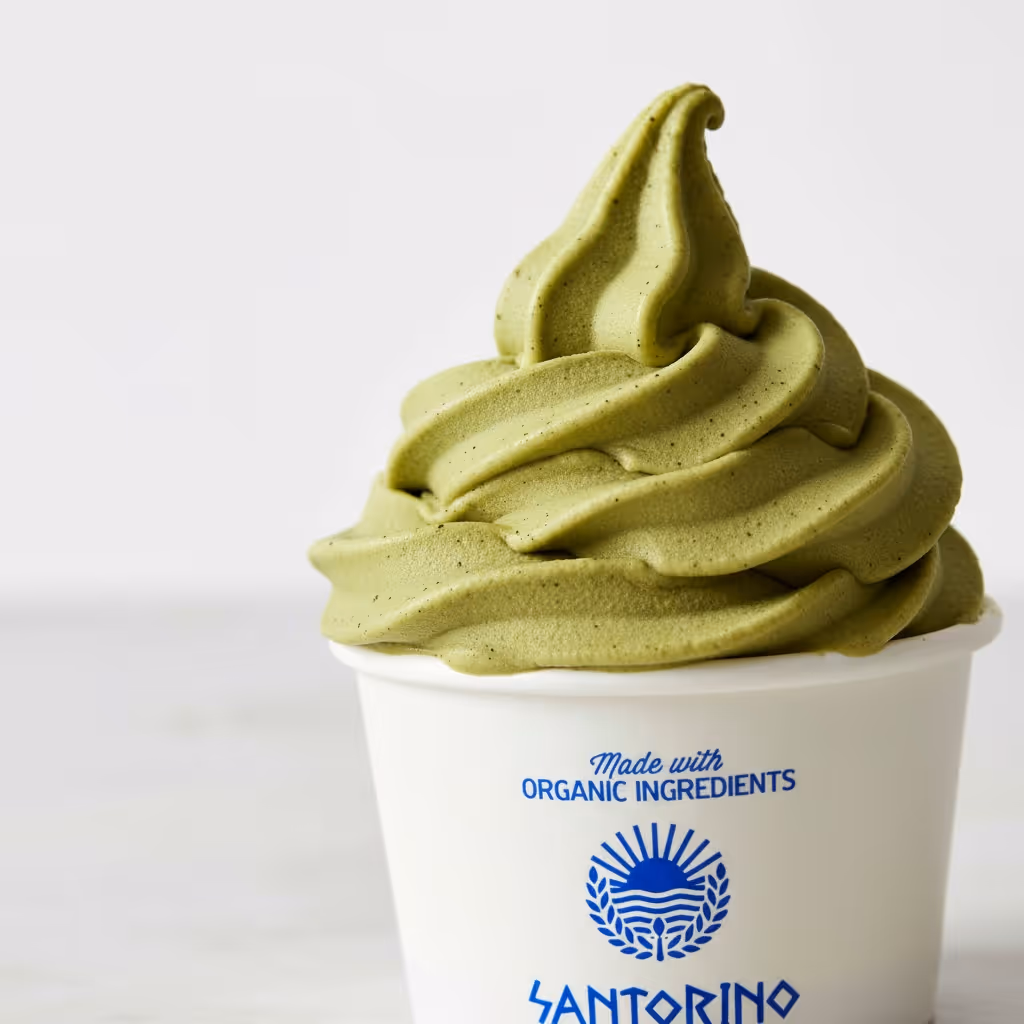 A cup of green matcha soft serve frozen yogurt in a white cup labeled Santorino with organic ingredients.