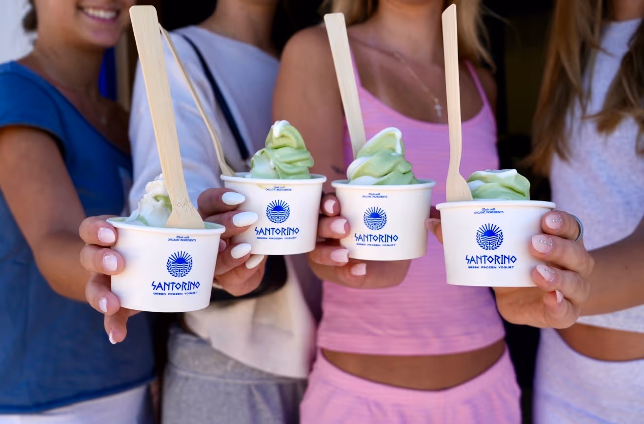 Four people holding cups of green and white Santorino Greek frozen yogurt with wooden spoons.