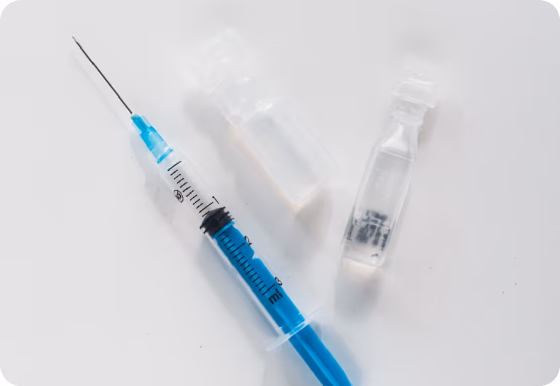 Syringe filled with blue liquid beside two clear medical vials on a white surface.