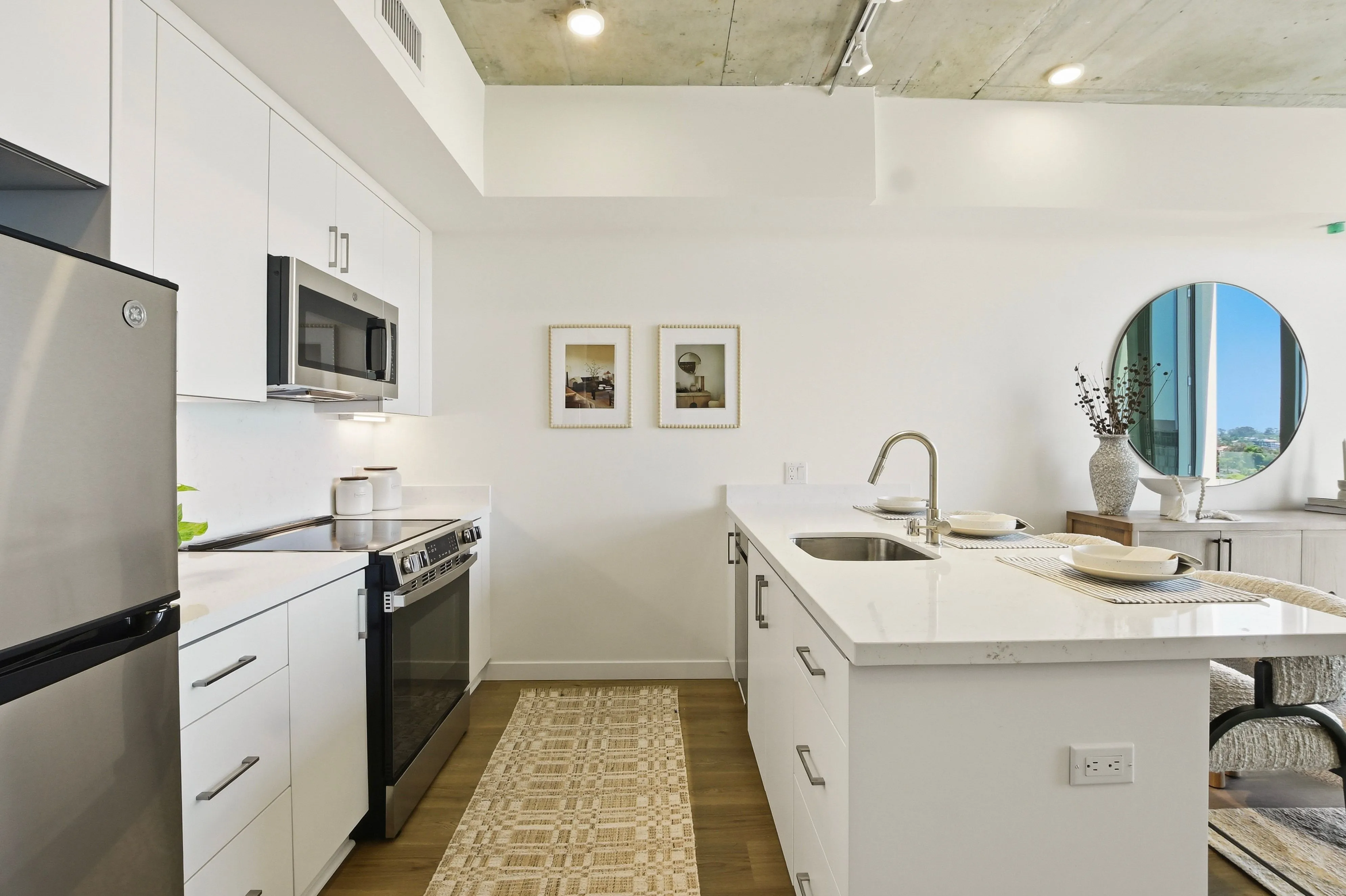 Modern kitchen with white cabinets, stainless steel appliances, island sink, table settings, and round mirror.