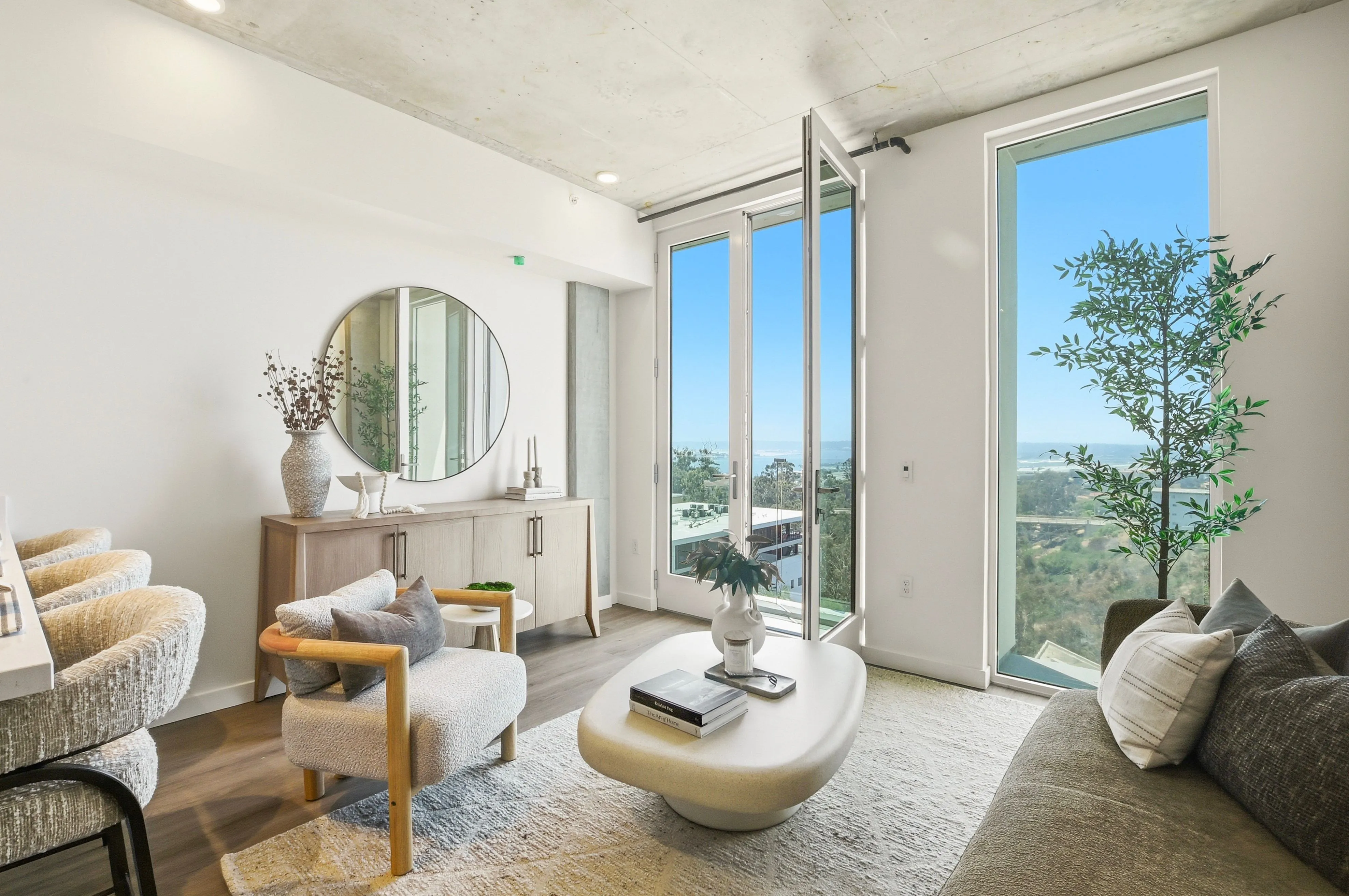 Bright living room with modern furniture, large window, open glass door, and scenic outdoor view.