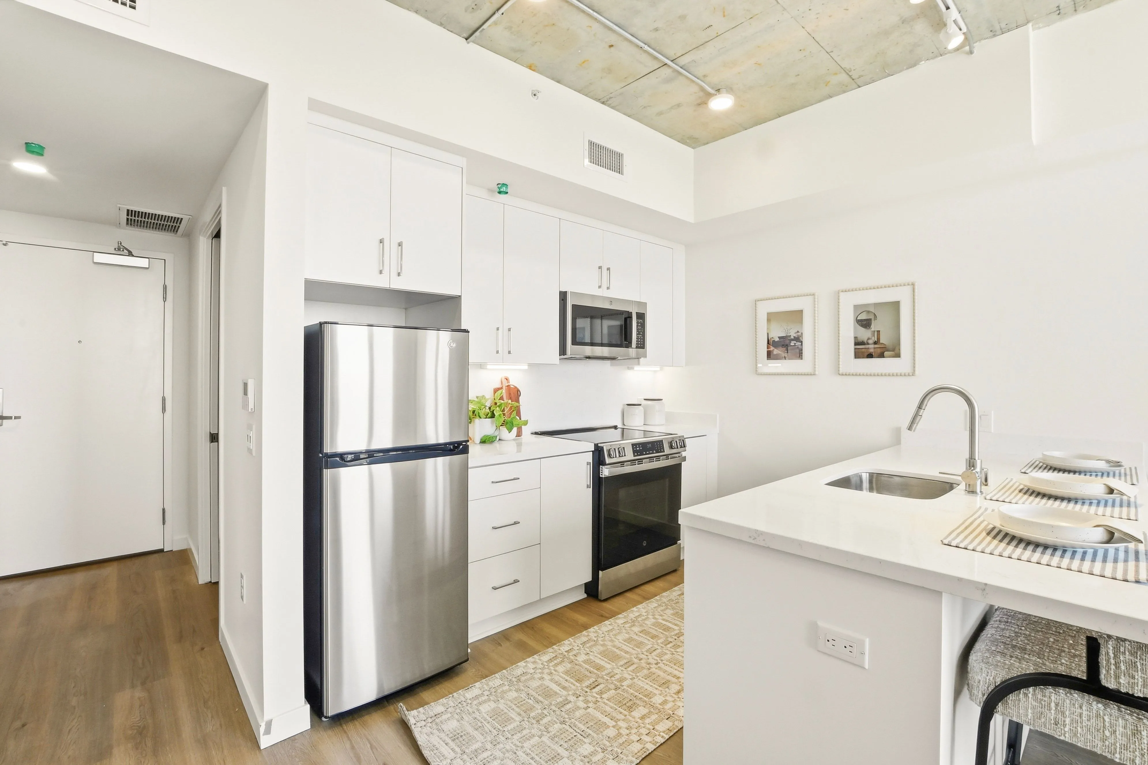 Modern kitchen with stainless steel fridge, oven, microwave, white cabinets, island with sink, and bar stools.