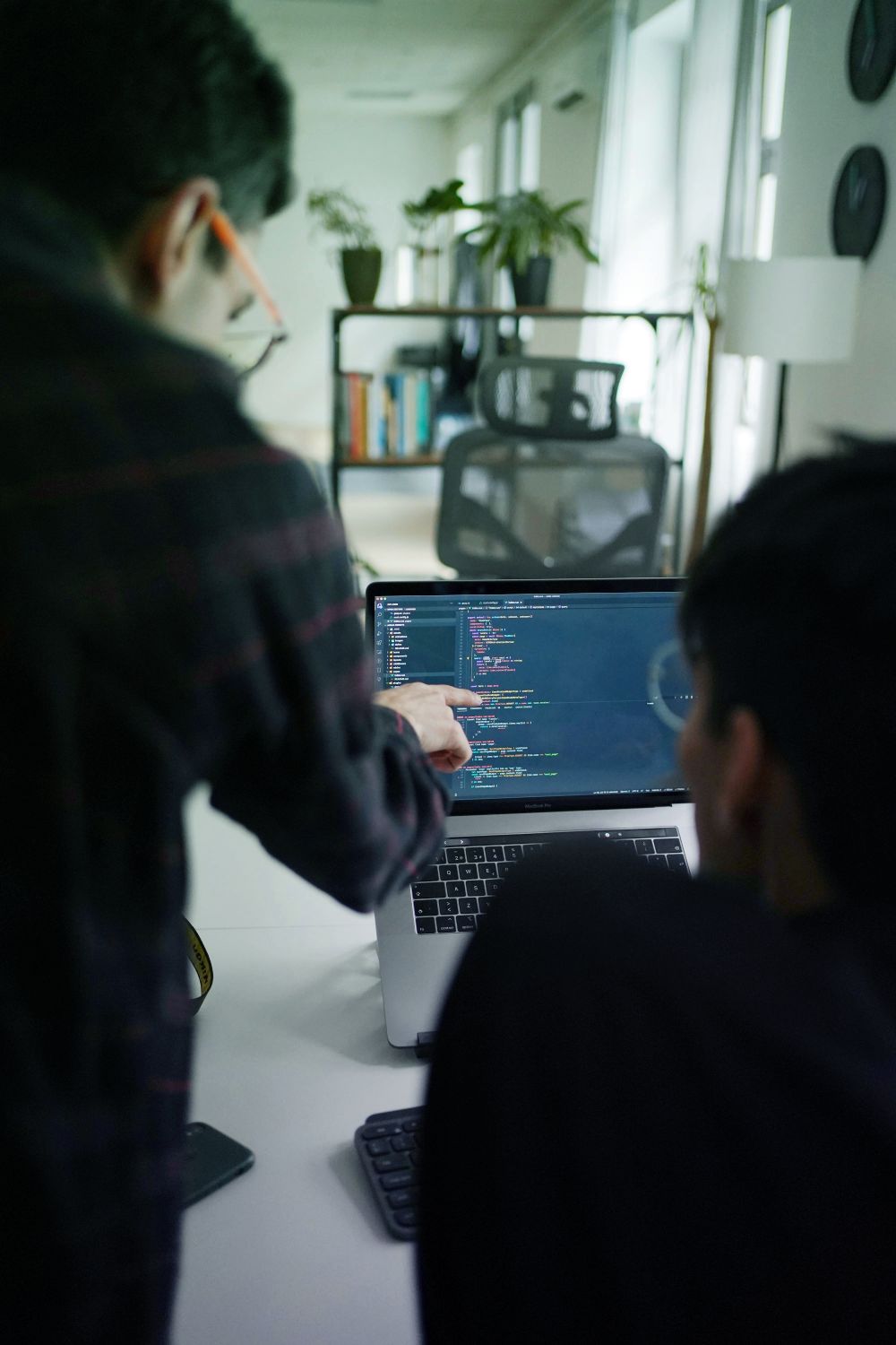 Two developers reviewing and discussing code on a laptop screen in a modern office.