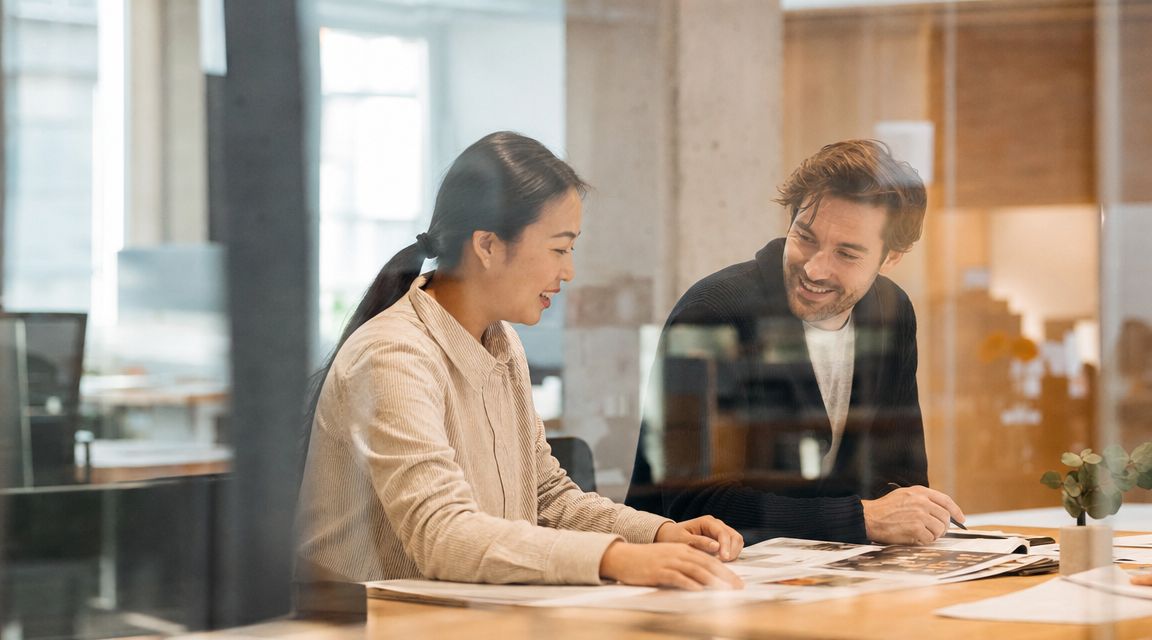 A professional woman and man collaborating on documents at a bright modern office table.