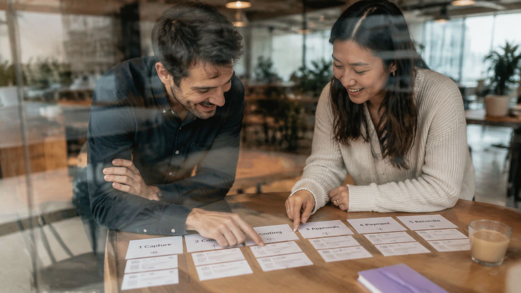 A man and a woman collaborating on business process flow charts at a wooden table in office.