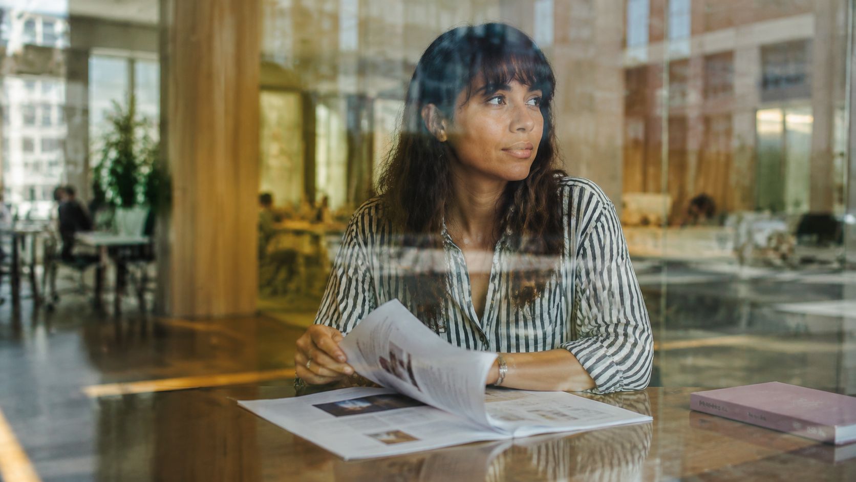 A woman with dark hair in a striped shirt reads a document at a glass-topped table.