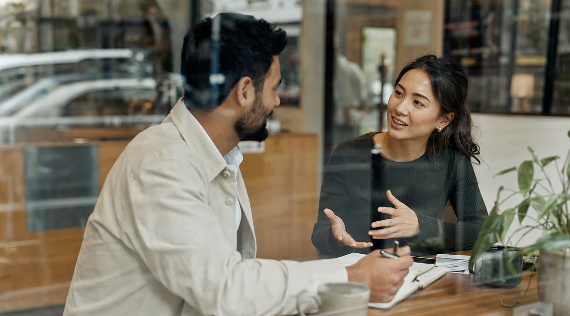 A professional man and woman having a productive discussion while sitting at a wooden table together.