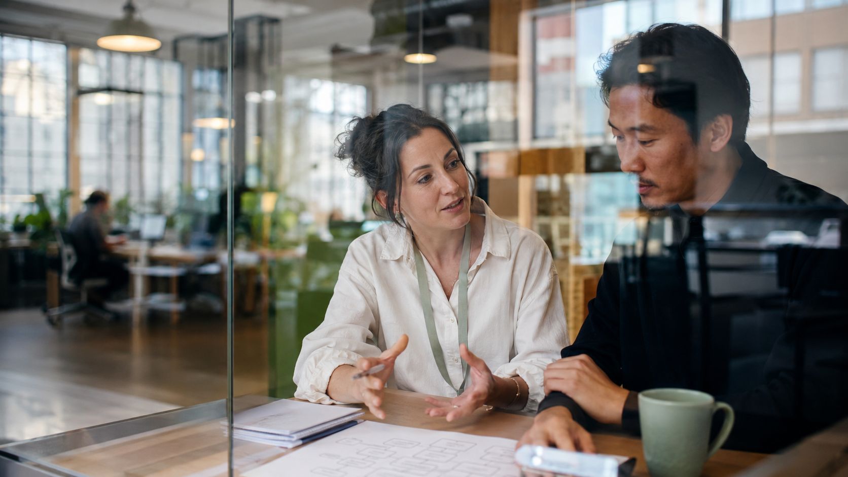 A professional woman and man collaborating on a business project in a modern, glass-walled office space.