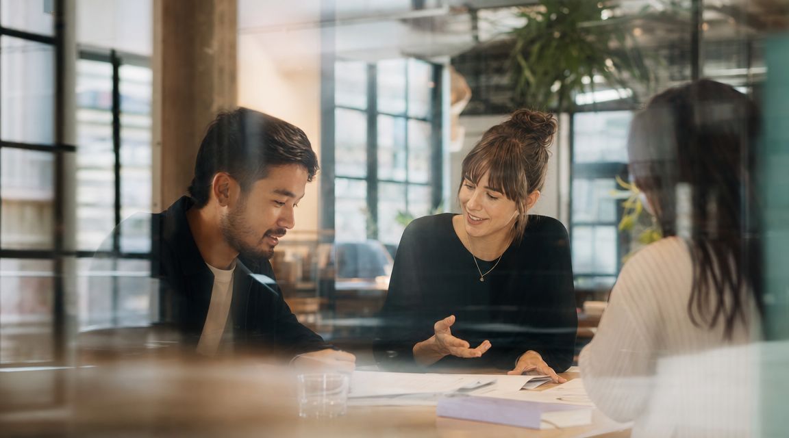 A diverse team of professionals collaborating on documents at a table in a bright modern office space.
