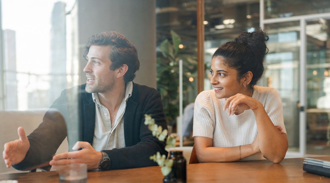 A professional man and woman having an engaging business discussion at a table in a modern office.