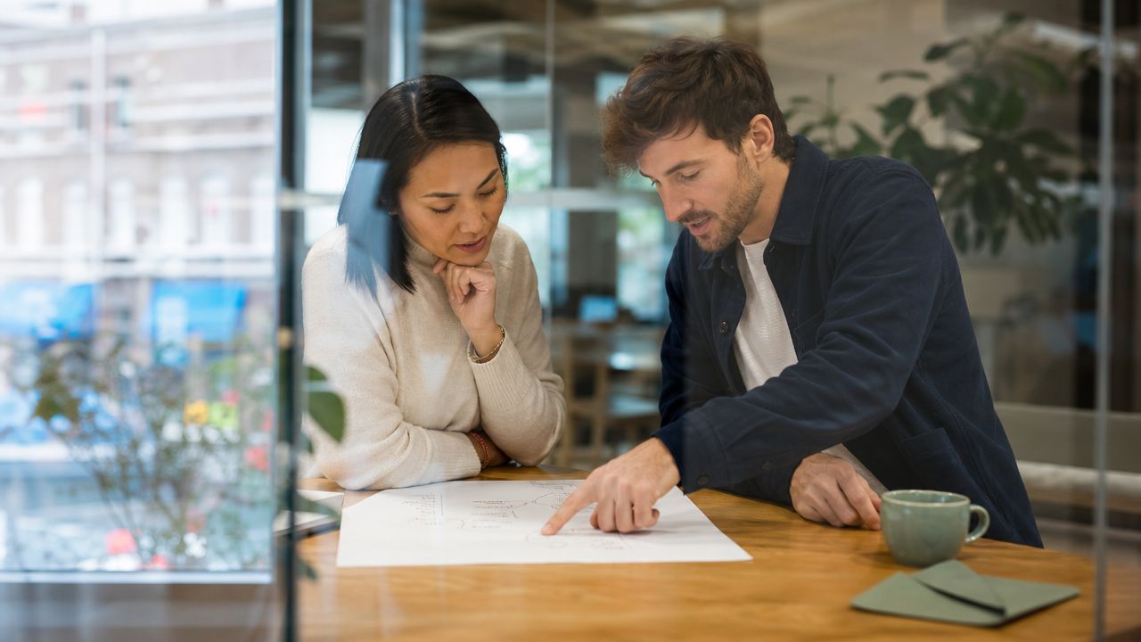 A professional man and woman collaborating on a business strategy project over a document in an office.