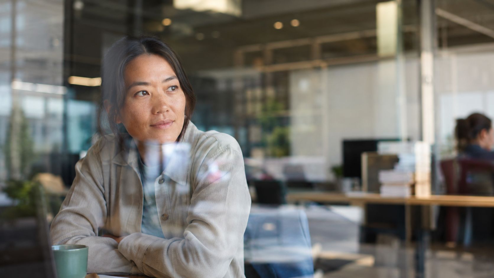 A professional woman working in a modern office space, viewed through a glass window partition.