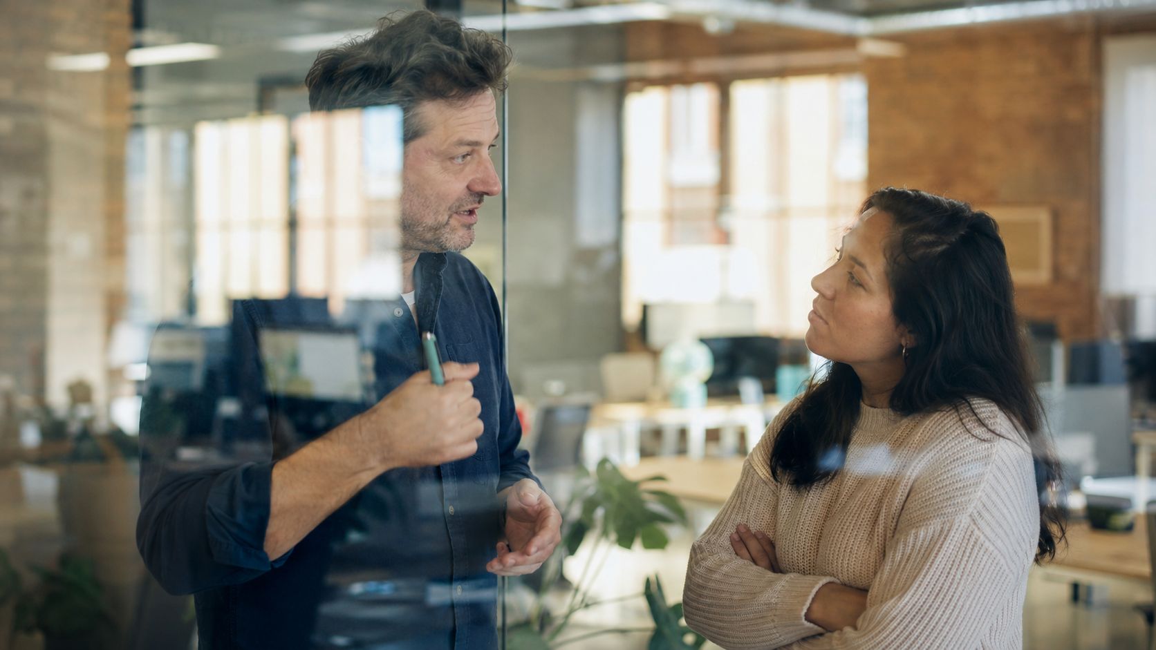 A professional man and woman discussing business strategy in a modern, light-filled office through glass walls.