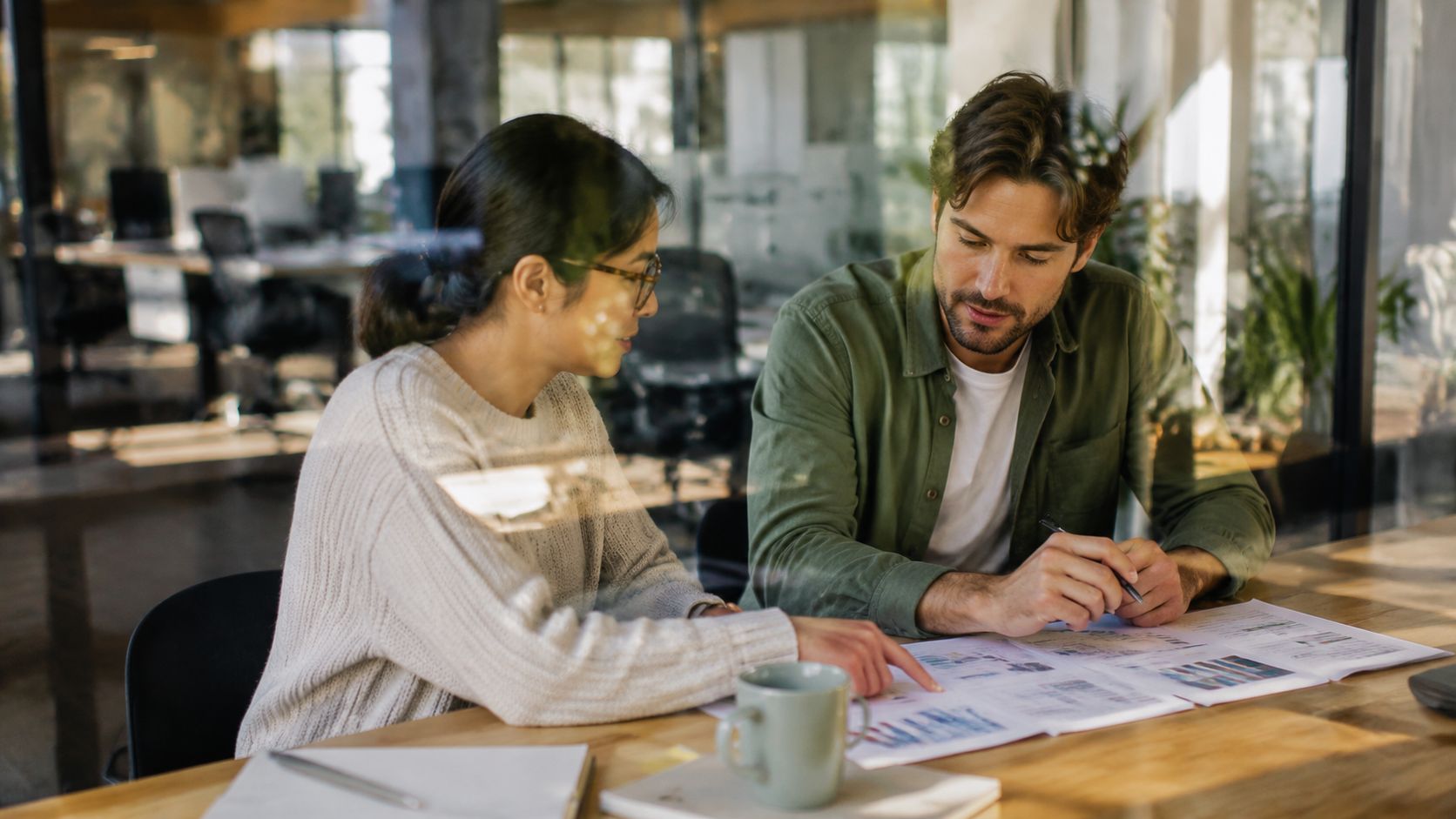 A woman and a man collaborating and reviewing financial charts together at a wooden office table.